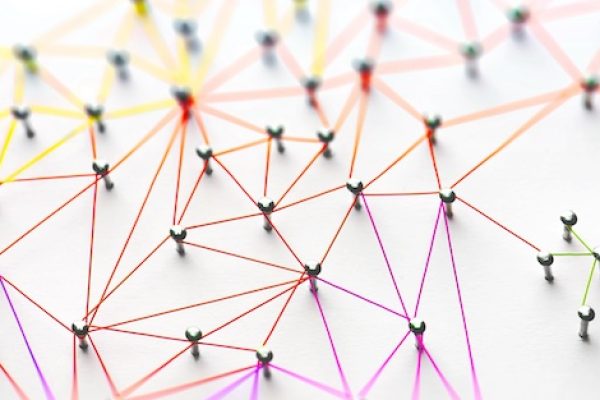 Linking entities. Networking, social media, SNS, internet communication abstract. Small network connected to a larger network. Web of red, orange and yellow wires on white background. Shallow DOF.